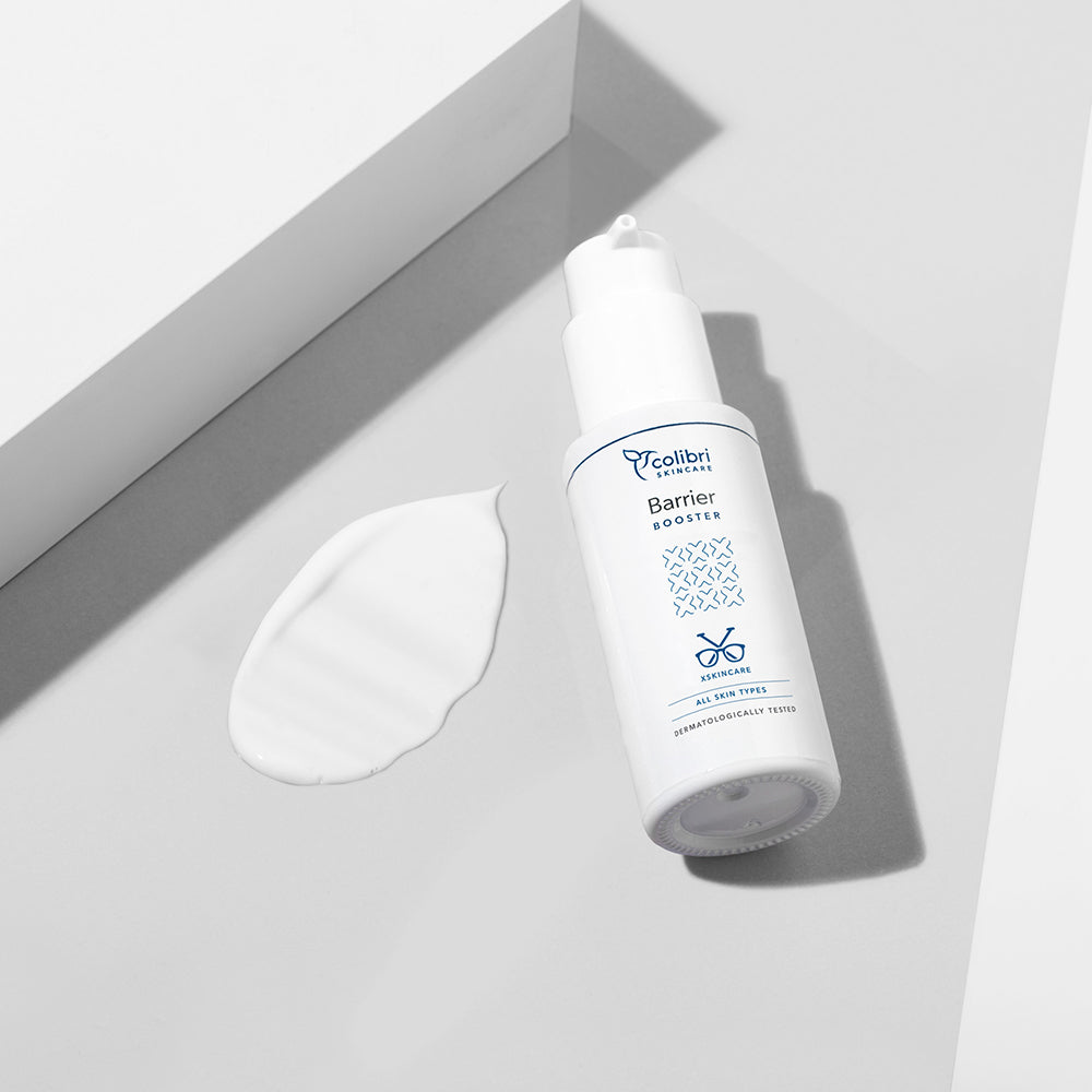 Weiße Flasche eines Barrier Boosters mit blauer Schrift und daneben ein Klecks der Creme auf grauem Hintergrund.