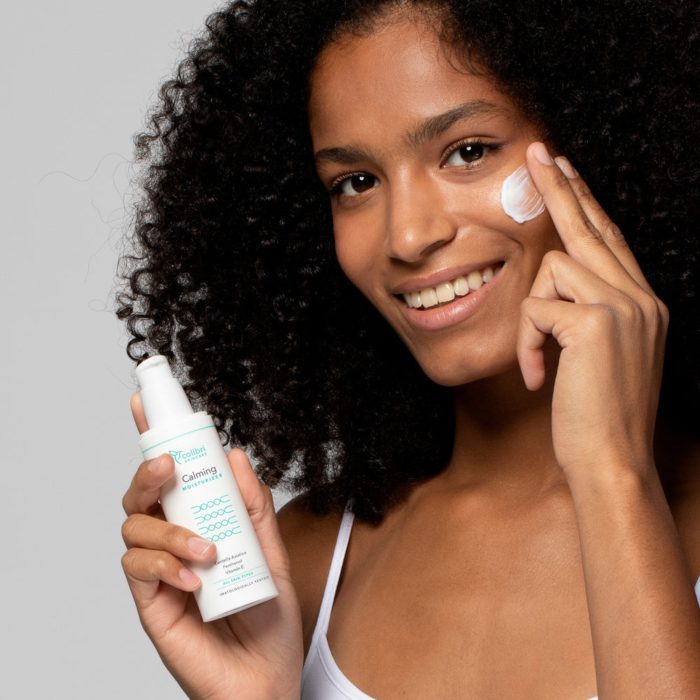 Frau mit lockigem Haar trägt Feuchtigkeitscreme auf, während sie eine Lotionflasche hält und lächelt.