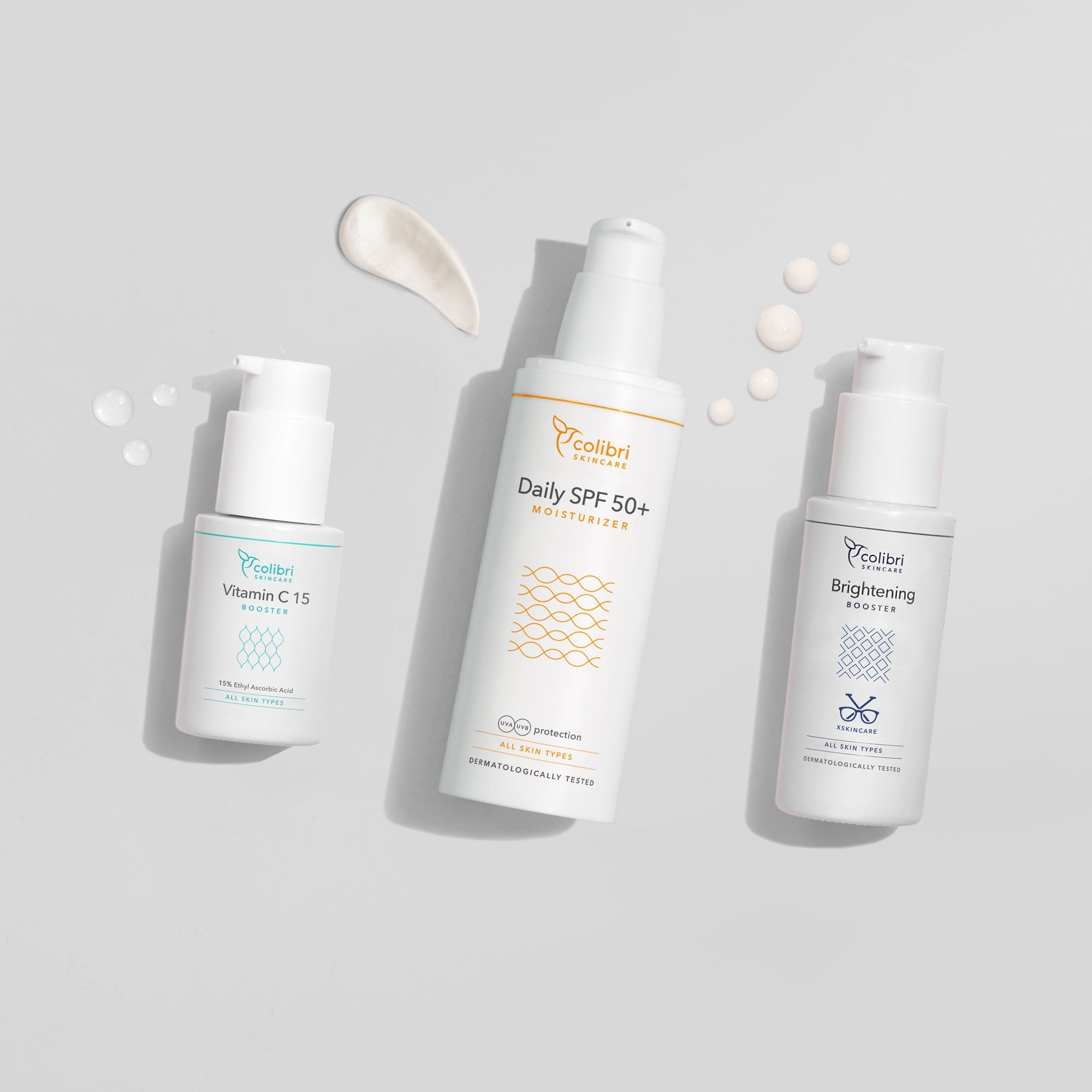 Drei Hautpflegeprodukte mit Vitamin C, SPF 50+ Feuchtigkeitscreme und Aufhellungsbooster auf grauem Hintergrund.