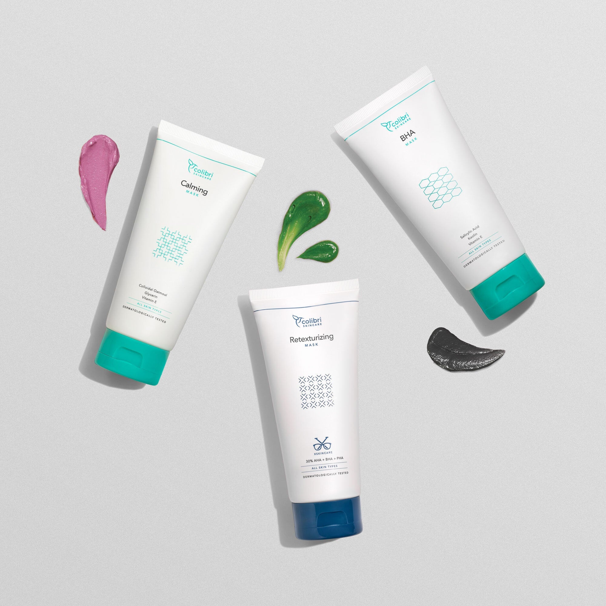 Drei Tuben Hautpflegeprodukte mit bunten Cremeklecksen auf einer grauen Oberfläche arrangiert.