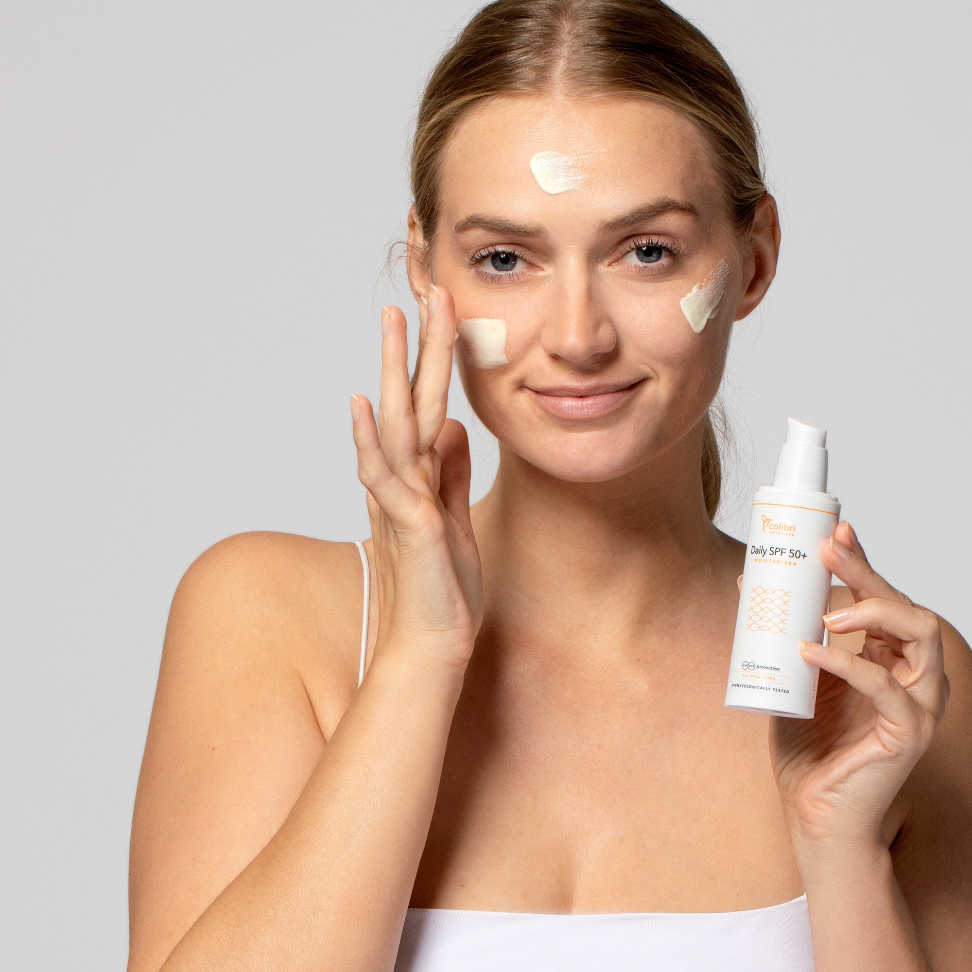 Frau trägt Sonnencreme auf ihr Gesicht auf und hält eine Flasche mit der Aufschrift "Daily SPF 50+."