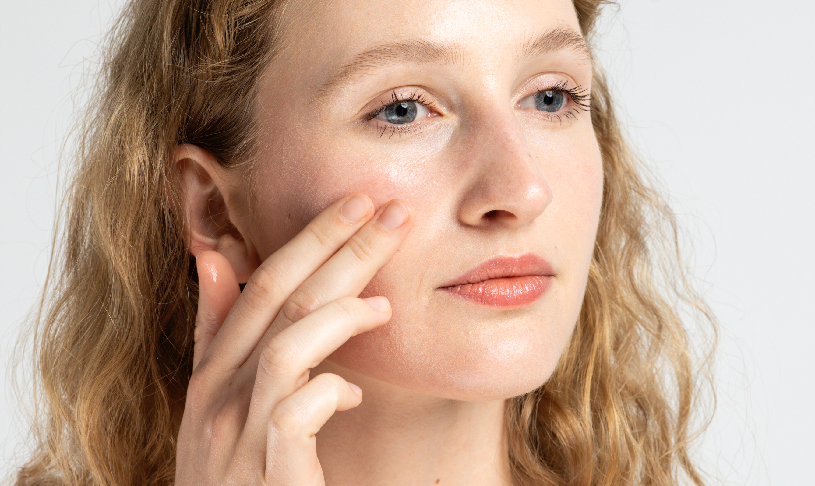 Eine Frau trägt mit zwei Fingern Creme auf ihre Wange auf.