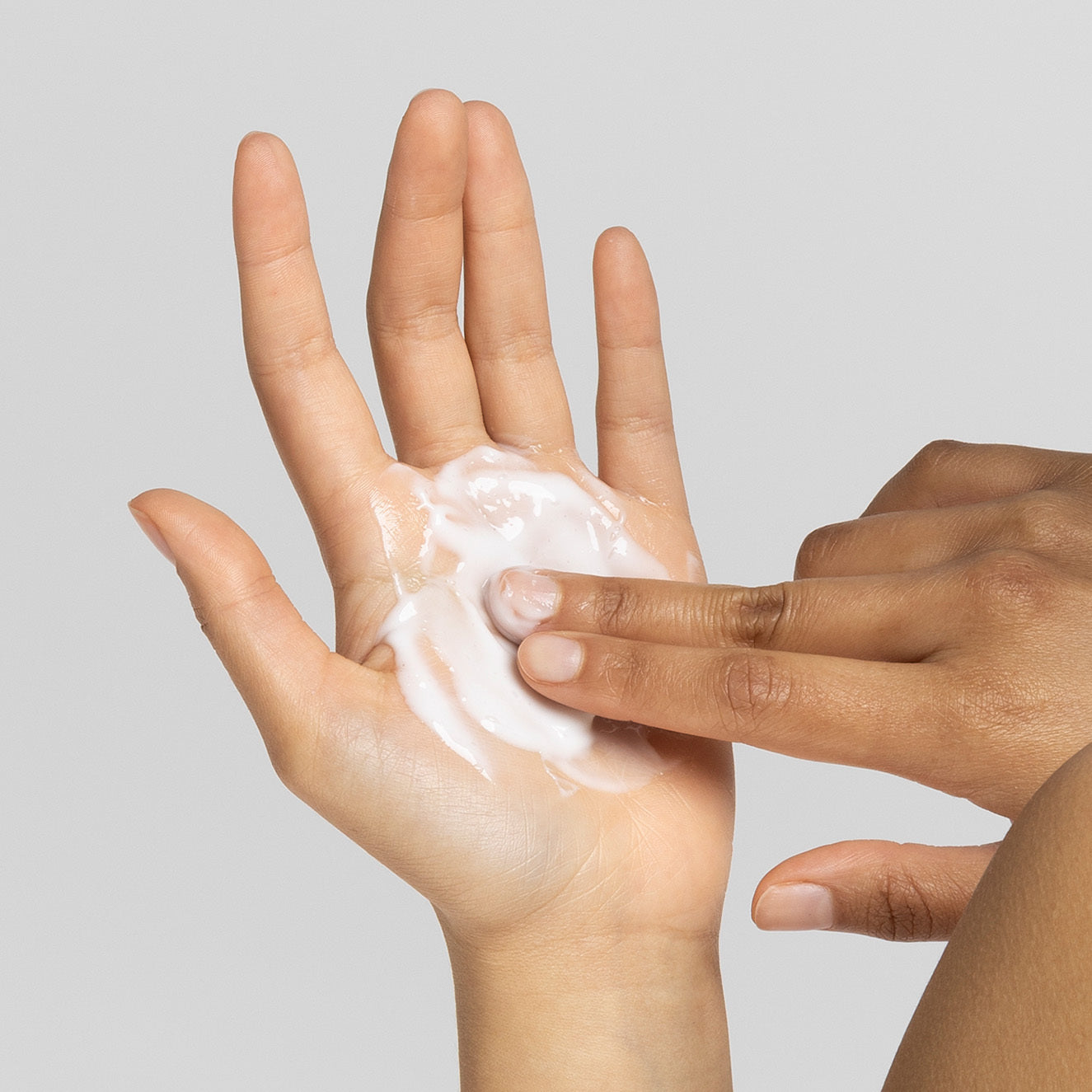 Eine Hand mit weißer Creme in der Handfläche, die mit einem Finger verteilt wird.