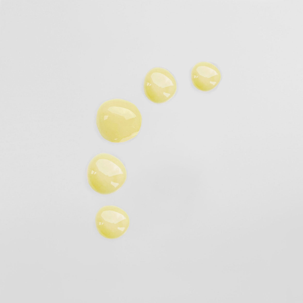 Fünf gelbe Flüssigkeitstropfen auf einer weißen Oberfläche.
