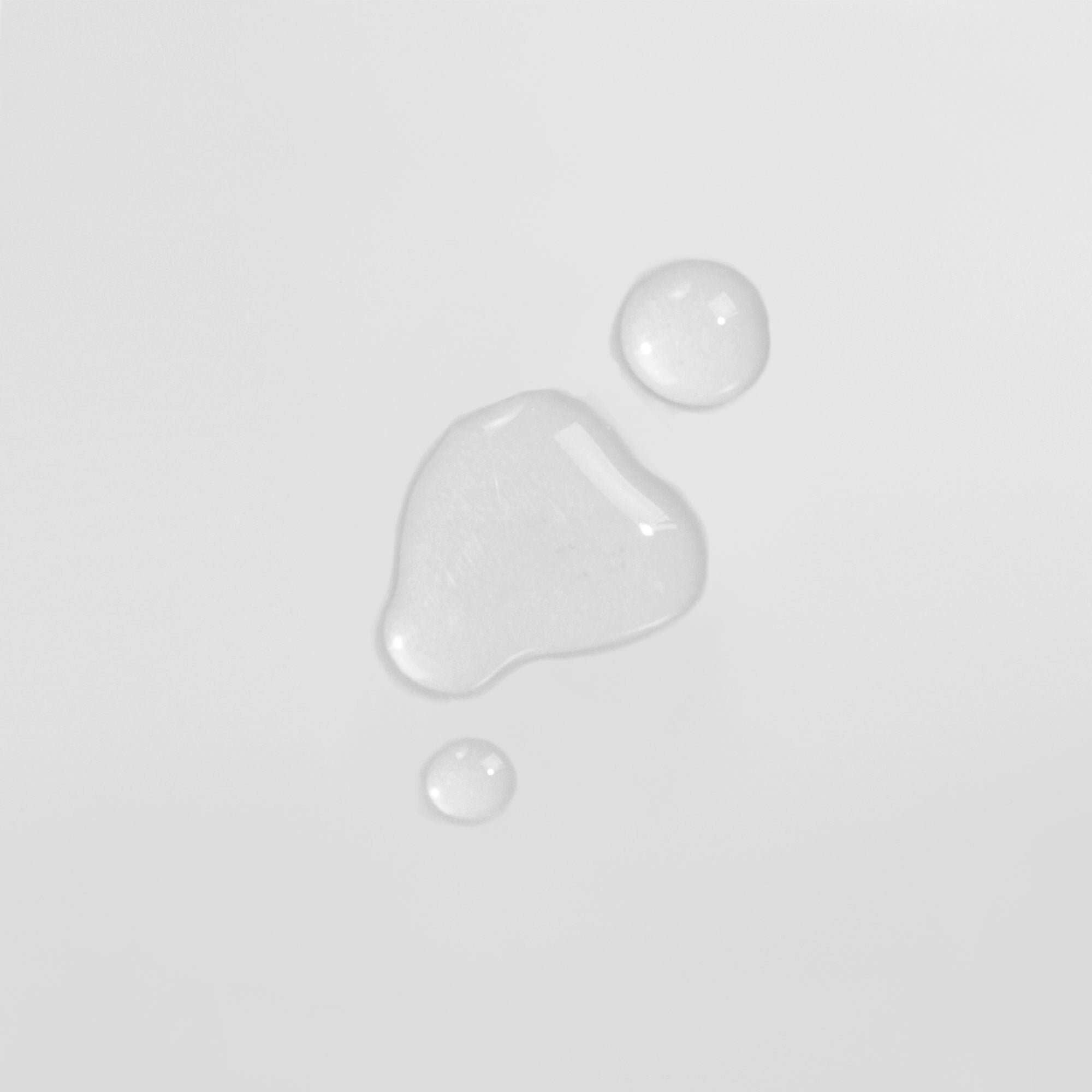 Drei transparente Wassertropfen auf einer weißen Oberfläche.