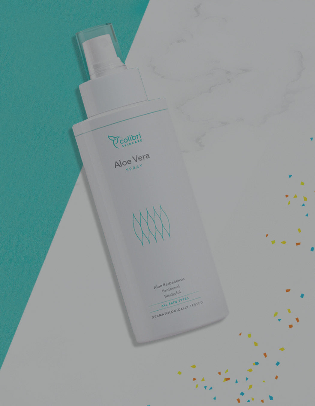 Sprühflasche Aloe Vera Spray auf weißem Hintergrund mit buntem Konfetti und türkisem Farbfeld, dermatologisch getestet.