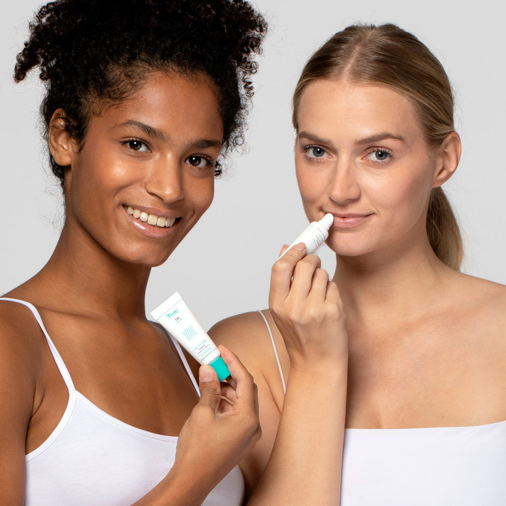 Zwei Frauen in weißen Tops halten Tuben mit Hautpflegeprodukten und lächeln in die Kamera.