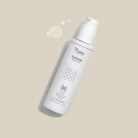 Weiße Flasche eines Exfoliate Boosters auf beigem Hintergrund mit einigen Tropfen daneben.