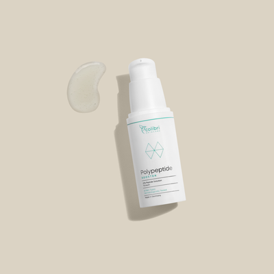 Flasche des Polypeptid-Boosters auf beigem Hintergrund, daneben ein Tropfen der Flüssigkeit.